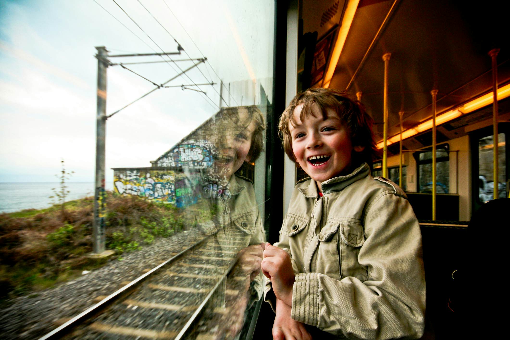 A very excited young boy looks out of a train window.